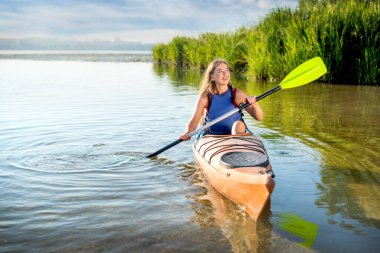 young attractive woman paddling a kayak on a lake with reeds. A girl in a canoe on a water excursion, active pastime
