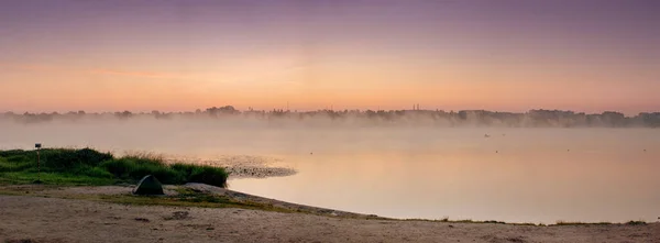 panorama of the shore of the lake at dawn with fog on the water