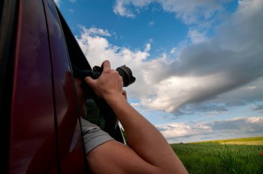 Summer trip. A man with a camera takes pictures of natural landscapes and a beautiful sky from the car window.