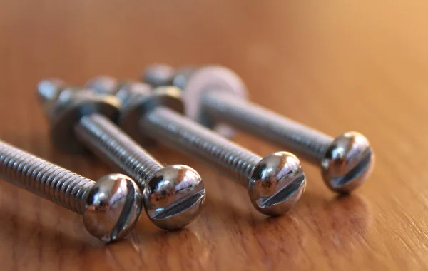 Tahta arka planda fındık ve çamaşır makineli dört uzun, krom kaplama vida. Quatro parafusos longos, cromados, com porcas e arruelas, sober um fundo de madeira.