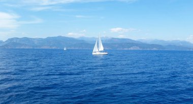 Mavi denizde beyaz bir yelkenli yüzüyor. Sessiz, huzurlu, rahatlatıcı bir manzara ve arka plan..