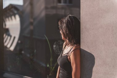 Siyah elbiseli siyah saçlı bir kadın pencerede poz veriyor. Kadın siyah güneş gözlüğü takıyor. Güzel, güneşli bir gün..