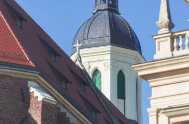 Fotoğraf çatıyı ve kilisenin bir kısmını gösteriyor. Başka bir binanın başka bir parçası bileşimi engelliyor. Bu binalar kasaba meydanında yer alıyor. Güneşli bir gün..