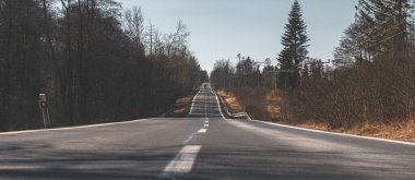 Arka planda görünen bir kamyoneti olan düz, uzun bir yol. Yol boyunca ağaçlar ve ızgaralar var. Hava güneşli ve gökyüzü bulutsuz..