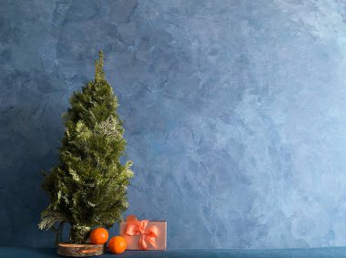 Mavi duvar sıva üzerinde hediye ve mandalinalı minyatür Noel ağacı.