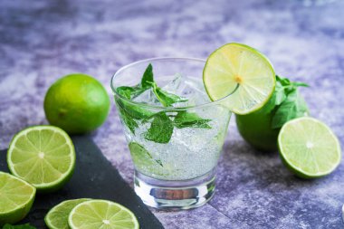copa de mojito con hielo , menta y lima listo para tomar frio, foto sobre mesa de marmol y fondo de madera