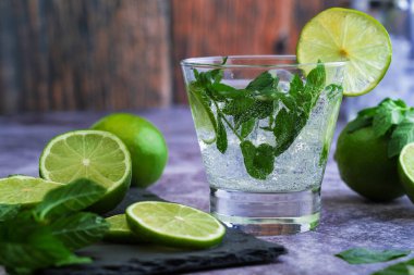 copa de mojito con hielo , menta y lima listo para tomar frio, foto sobre mesa de marmol y fondo de madera