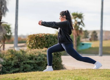 Mujer joven y atractiva consultando el mvil en un parque mientras hace yoga y expte al aire libre