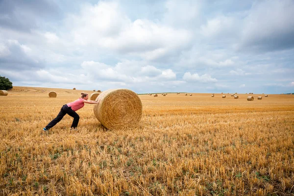 Young woman pushing in a field of straw bales — Stock Photo, Image