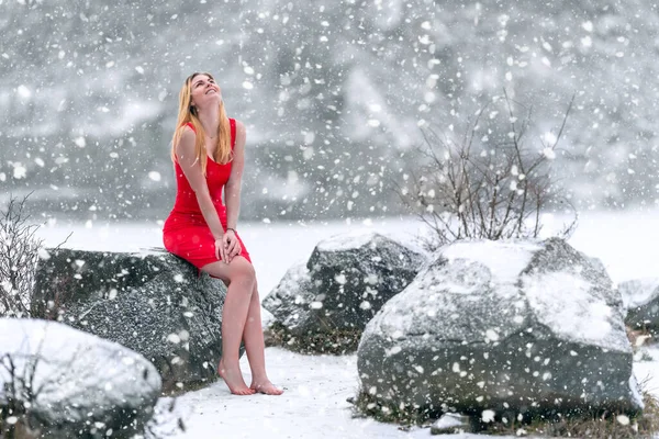 Ung vacker kvinna i röd klänning vid den snöiga frusna sjön på vintern — Stockfoto