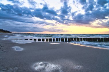 Baltık Denizi sahilinde gün batımı. Sahildeki yansıma. Groyne 'ler denize ulaşıyor. Gökyüzünde bulutlar olan mavi saat. Zingst 'te manzara fotoğrafı