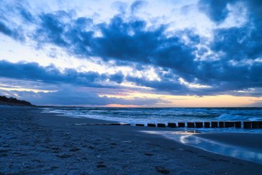 Baltık Denizi sahilinde gün batımı. Groyne 'ler denize ulaşıyor. Gökyüzünde bulutlar olan mavi saat. Zingst 'te manzara fotoğrafı