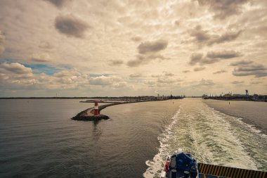 Lighthouse at Rostock harbor during departure by ship to Scandinavia. Calm Baltic Sea with clouds in the sky.