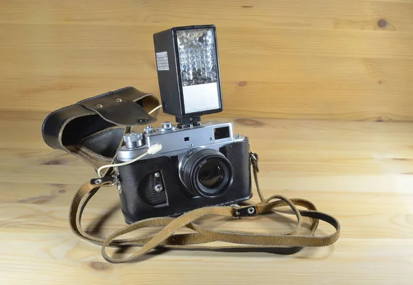 木製の背景に革ケースにオンカメラフラッシュと古いフィルムカメラ — ストック写真