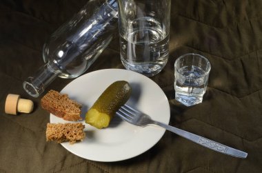  Çatalda salatalık turşusu, bir şişe votka, bir bardak votka, çavdar ekmeği, kahverengi arka planda beyaz bir tabak..