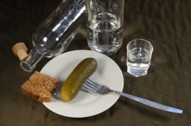  Çatalda salatalık turşusu, bir şişe votka, bir bardak votka, çavdar ekmeği, kahverengi arka planda beyaz bir tabak..