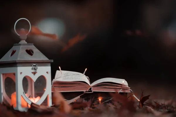 Leafs fall on the book and lantern with candles and lights during warm colorful autumn evening,september