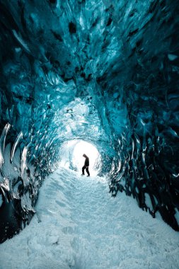 Kışın İzlanda 'nın Vatnajkull buzulunda güzel bir buz mağarasında duran insan.