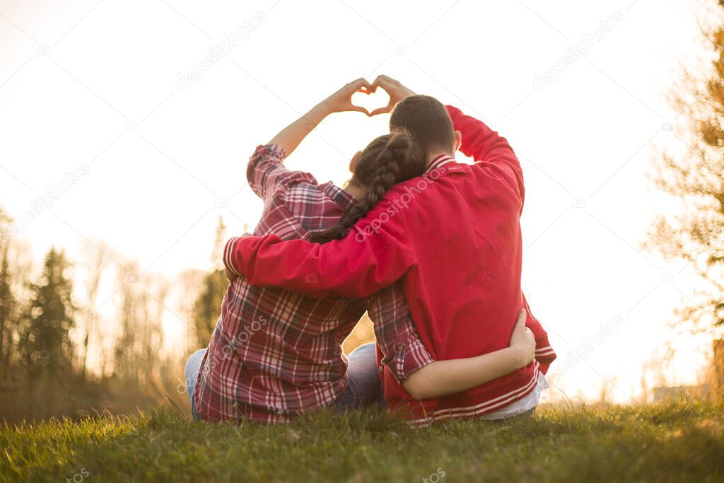Beautiful relationship between boy and girl, women and men. Love is in the air. They are in love. I love you. Two persons showing heart by hands in amazing summer sunset warm light. 