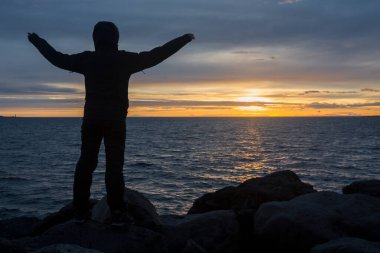 Hayatın tadını çıkar! Kız, Reykjavik, İzlanda yakınlarında okyanusun arkasında inanılmaz bir günbatımının keyfini çıkarıyor.