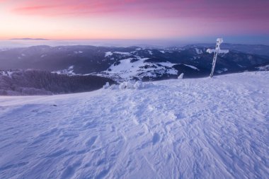Dondurucu kış mevsiminde dağın tepesinde haçla muhteşem renkli bir gün doğumu, Zvolen, Big Fatra, Slovakya