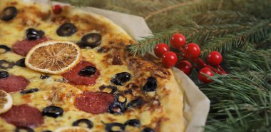 Ahşap masanın üzerinde köknar dalları ve zeytinlerle süslenmiş küçük bir noel pizzası. portakal ve sosis.