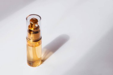 Üzerinde kozmetik serumu olan şeffaf bir şişe ya da beyaz arka planda metni olan gölgeli bir yağ.