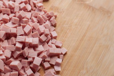 Ahşap bir kesme tahtasının üzerinde ince dilimlenmiş pembe renkli haşlanmış sosis. Bulanık kenarlı ve yazı yazılacak bir yer var.