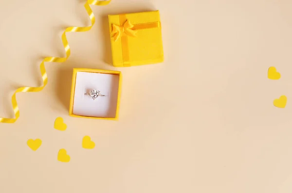 黄色のリボンと黄色の紙の心を持つベージュの背景に黄色のギフトボックスに白い金のリングテキストのための場所 — ストック写真