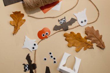 Balkabaklarından, yarasalardan ve hayaletlerden yapılmış bir halat üzerinde ev yapımı çelenk bej bir arka planda renkli kağıt, yaprak ve göz kırıntılarının yanında gözler