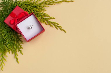 Beyaz altın bir yüzük. Kırmızı bir kutuda büyük bir taş. Bej bir arka planda.