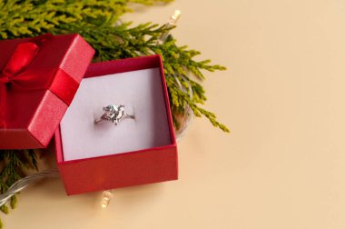 Yeşil bir thuja dalının arka planında kırmızı bir kutuda büyük bir mücevher olan beyaz bir altın yüzük ve neşeli bir çelenk.