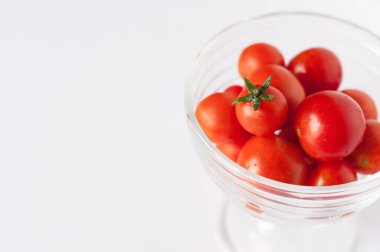 Cam bardakta küçük kırmızı kiraz domatesleri. Beyaz arka planda, mesaj için bir yer var.