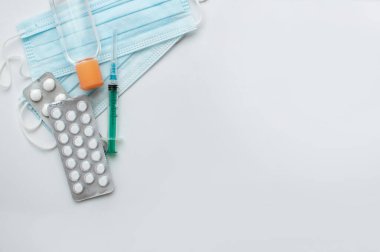 Tıbbi maskeler, antiseptik, tek kullanımlık şırıngalar ve haplar beyaz bir arkaplanda metinler için yer var.