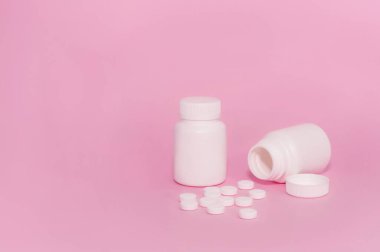 Pembe arka planda işaretlenmemiş iki ilaç şişesi ve dağınık haplar.