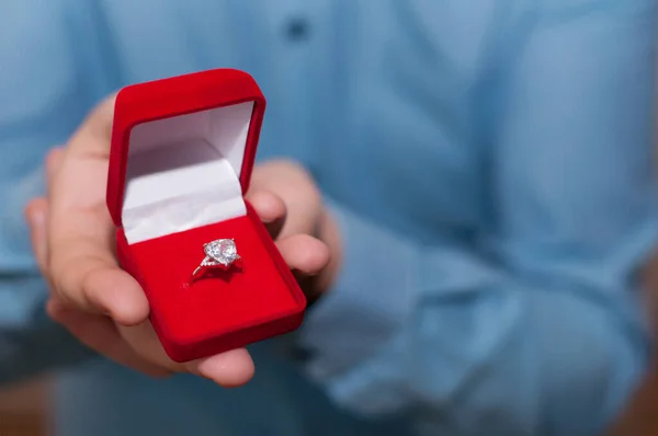 青いシャツを着た男の手に開いた赤いベルベットの箱の中に宝石のような白い金の指輪 — ストック写真