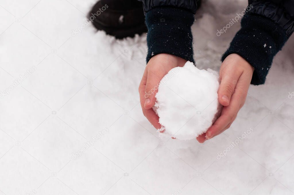 A ball of snow in the hands of a child on a white background