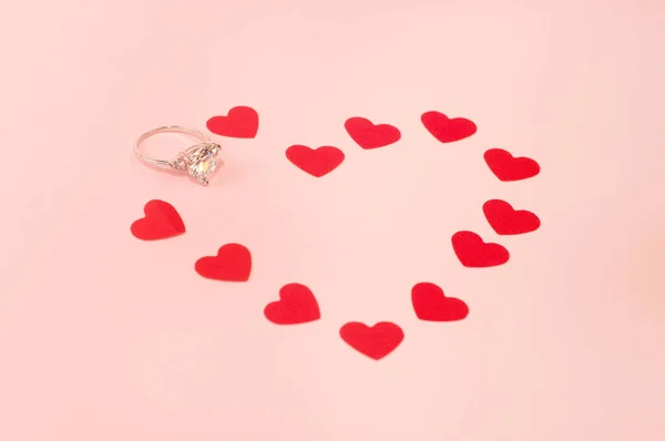 ピンクの背景にコンフェッティのハート型の宝石のついたホワイトゴールドのリング — ストック写真