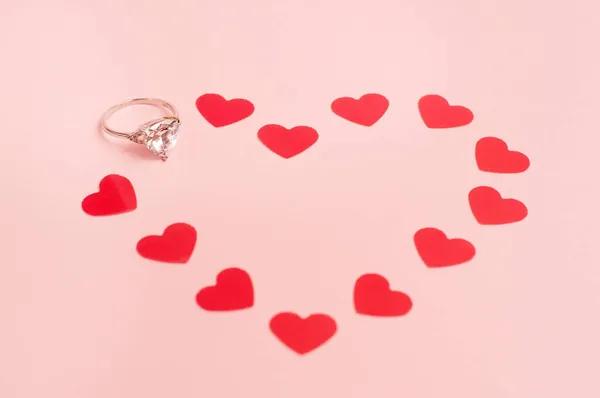 ピンクの背景にコンフェッティのハート型の宝石のついたホワイトゴールドのリング — ストック写真