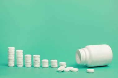 Bir bar çizelgesi şeklinde mavi arkaplan üzerinde beyaz tablet yığınları ve ön planda birkaç dağınık ve hafif bulanık tablet içeren beyaz bir kavanoz.