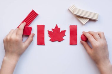 Kırmızı akçaağaç yaprağıyla Kanada bayrağı ve beyaz arka planda kırmızı ve beyaz renkli plasticine blokları olan bir çocuğun elleri