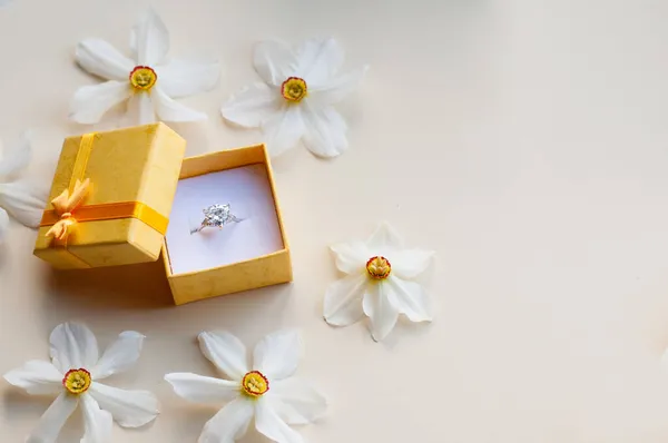 白い金の指輪のついた黄色い箱を開けて光を背景にダフォディの花をテキストのためのスペースで — ストック写真