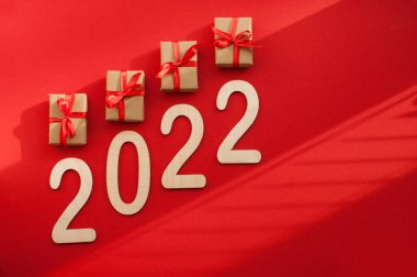 kırmızı kurdeleli el işi paketlemedeki hediyeler ve kırmızı arkaplandaki 2022 sayısı.