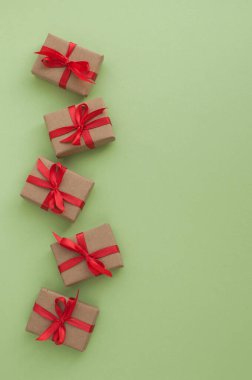 Yeşil arkaplanda kırmızı kurdeleli küçük hediyeler ve dikey formatta metin için boşluk