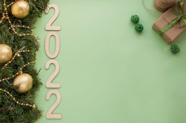 2022 rakamları yeşil arka planda, Noel ağacı dalları ve altın topların yanında ve yeşil kurdeleli bir hediye.