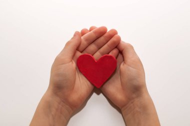 Beyaz arka planda, çocukların avuçlarında plastikten yapılmış bir kalp.