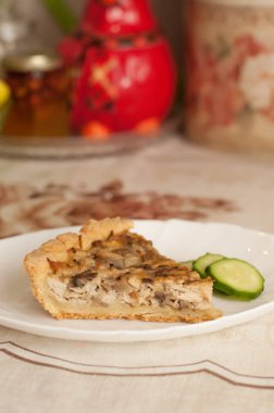 Tavuklu bir parça kish ve beyaz tabakta salatalık dilimli mantar.