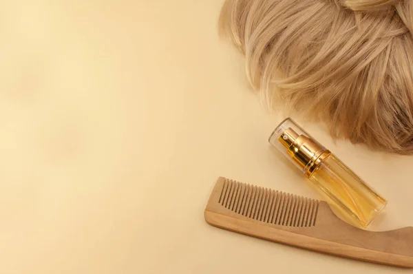 hair oil, wooden comb and blonde hair on beige background with space for text