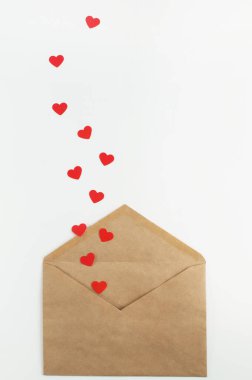 Beyaz arka planda bir zarftan kırmızı kağıt kalpler düşüyor.