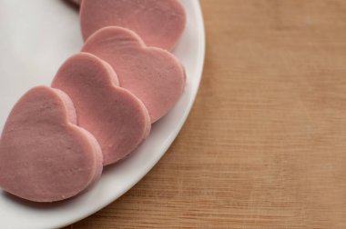 Ahşap bir arka planda beyaz bir tabakta kalp şeklinde kesilmiş sosis ve metin için bir yer.